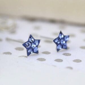 A pair of Sterling Silver - Crystal Blue Stars stud earrings on a polka dot background with Sterling Silver Crystal blue star studs.