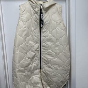 A white quilted vest hanging on a door.