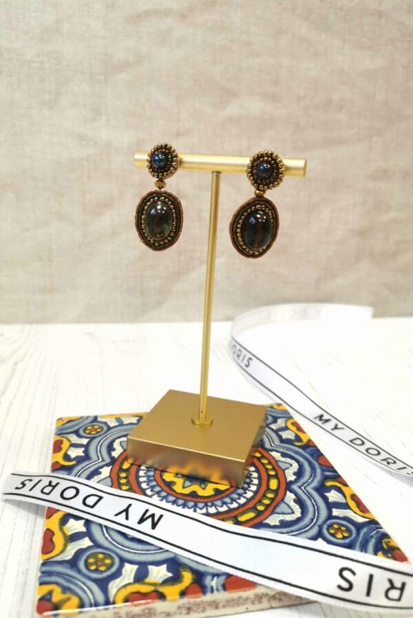 A pair of earrings on a stand with a ribbon.