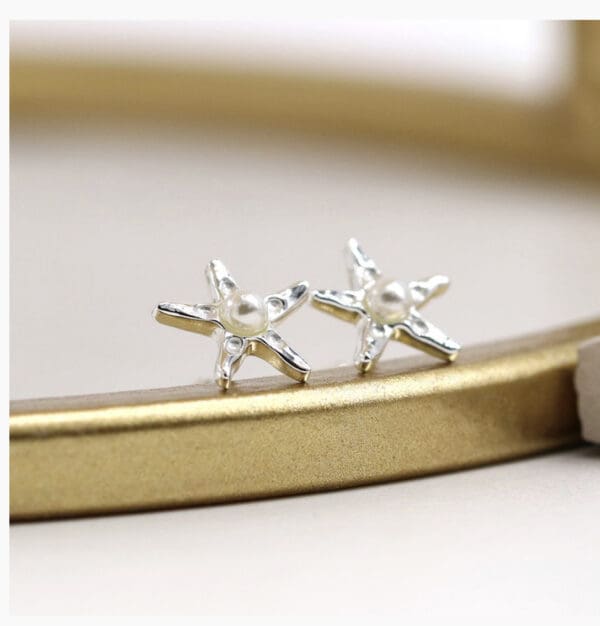 A pair of silver star stud earrings on a gold plate.