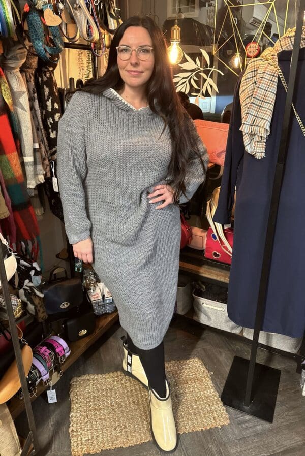 A woman in a grey sweater dress standing in a clothing store.