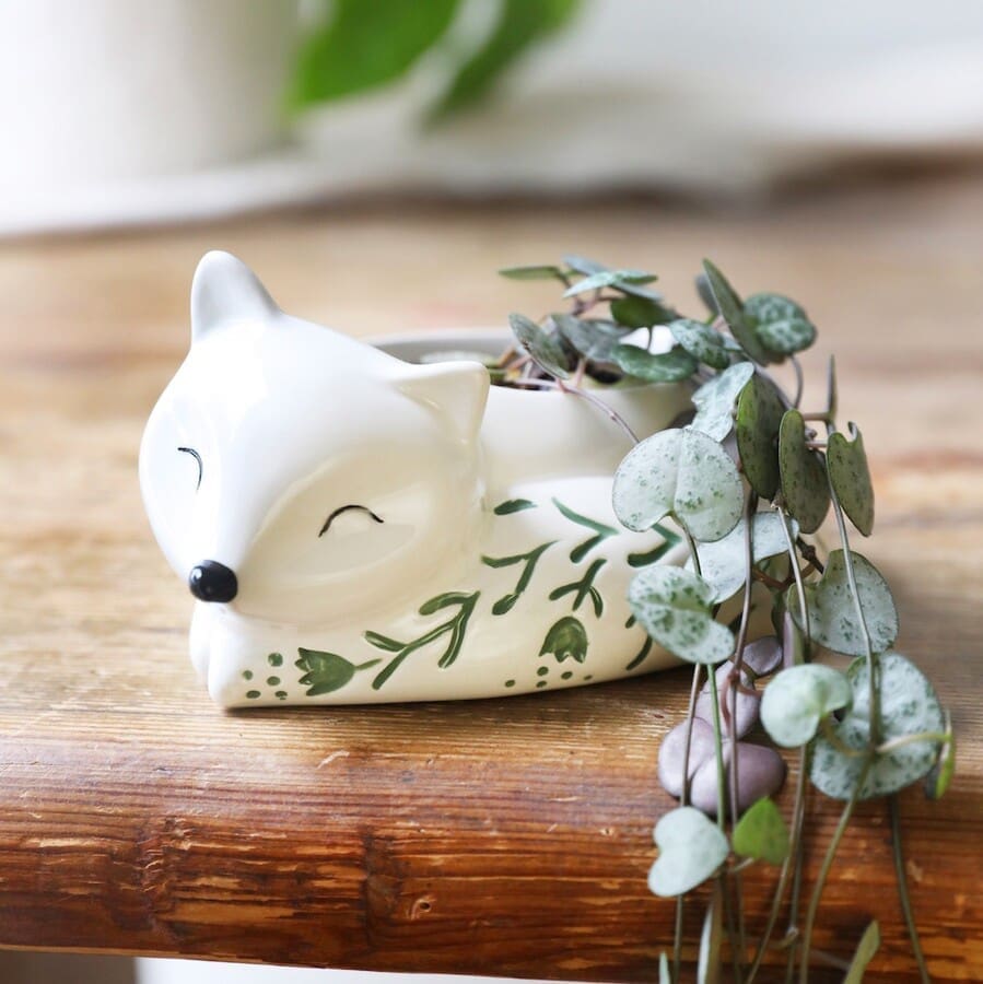 A ceramic fox planter sitting on a wooden table.
