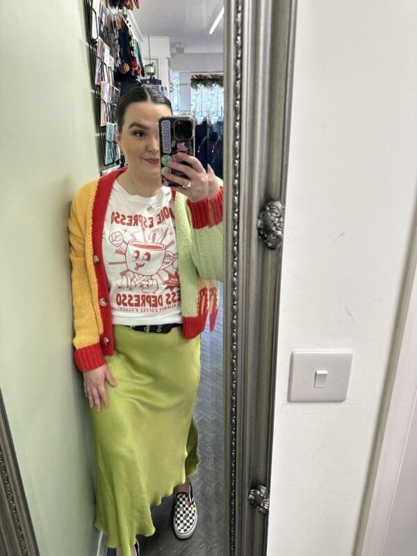 A woman, wearing a Satin Skirt in Lime, is taking a selfie in front of a mirror.
