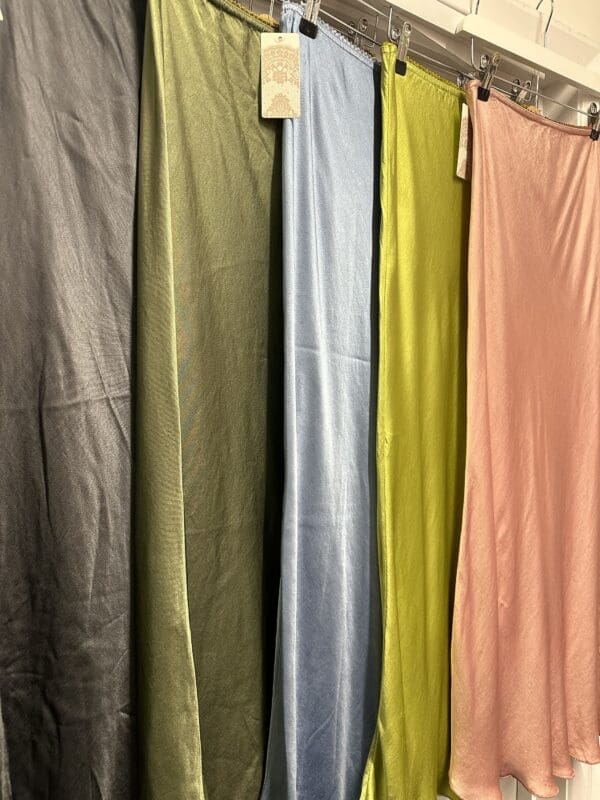 A group of different colored Satin Skirts in Lime, including a vibrant lime one, hanging on a rack.