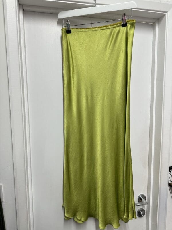 A Satin Skirt in Lime hanging on a door.