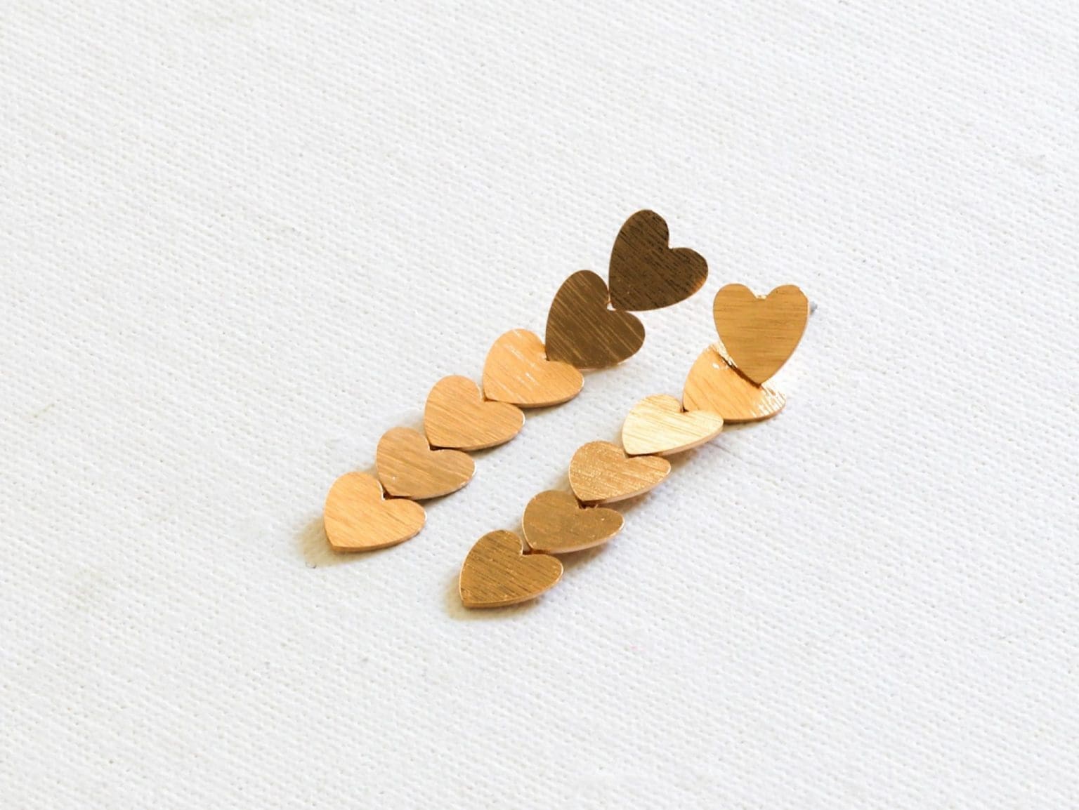 A pair of gold heart shaped earrings on a white surface.